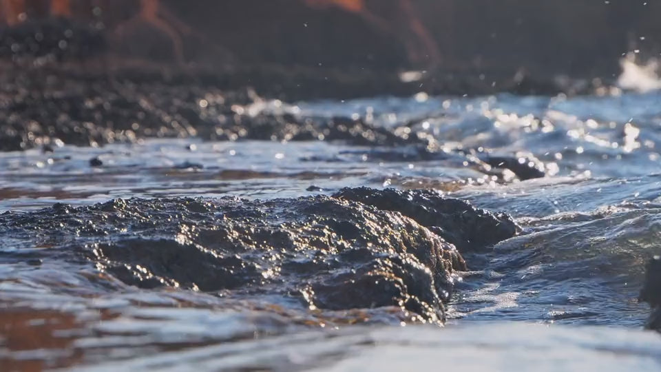 Videooptagelse af havets blå bølger, der bevæger sig rytmisk mod stranden under sollys.